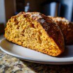 A close-up of a slice of sourdough pumpkin bread on a plate, showcasing its golden-brown crust and moist interior.