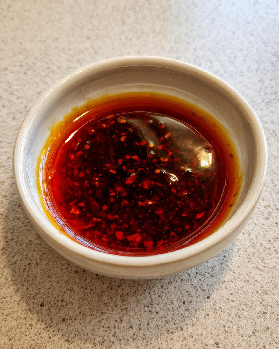 A close-up of a small bowl filled with vibrant red dumpling sauce, featuring visible chili flakes.
