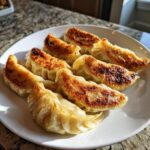 A plate of golden-brown, pan-fried Traditional Chinese Dumplings with crispy bottoms.