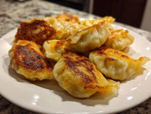 A close-up of golden-brown pan-fried Traditional Chinese Dumplings piled on a white plate, showcasing their crispy bottoms.