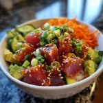 A close-up of a vibrant Tuna Poke Bowl featuring marinated tuna, avocado, cucumber, and shredded carrots on a bed of rice.