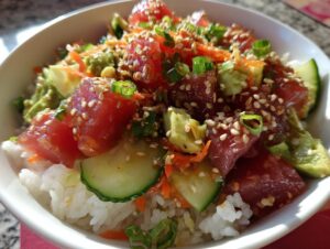 A vibrant Tuna Poke Bowl filled with cubed raw tuna, avocado, cucumber, shredded carrots, and sesame seeds over rice.