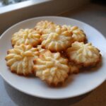 A close-up of a plate piled high with golden-brown whipped shortbread cookies, showcasing their delicate, star-like shape.