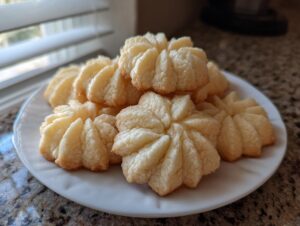 A plate of golden-brown whipped shortbread cookies with a delicate, star-like pattern.