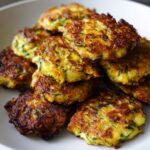 A close-up of a stack of golden-brown zucchini fritters, showing crispy edges and visible zucchini shreds.