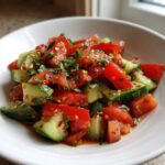 Close-up of a vibrant cucumber tomato salad tossed with herbs and spices in a white bowl.