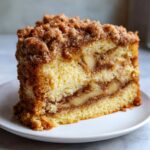 A thick slice of moist apple coffee cake featuring layers of spiced apples and a generous cinnamon streusel topping.