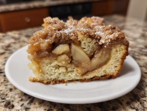 A close-up of a moist slice of apple coffee cake featuring tender baked apples and a cinnamon streusel topping.