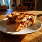 Two thick slices of amazing apple pie recipe showing flaky crust and cinnamon-spiced apple filling.