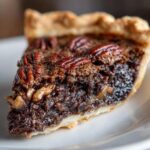 Close-up of a rich, dark slice of chocolate pecan pie showing the gooey filling and pecan topping.