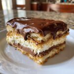 A decadent slice of eclair cake showing layers of cake, vanilla cream, chocolate pudding, and thick chocolate glaze.
