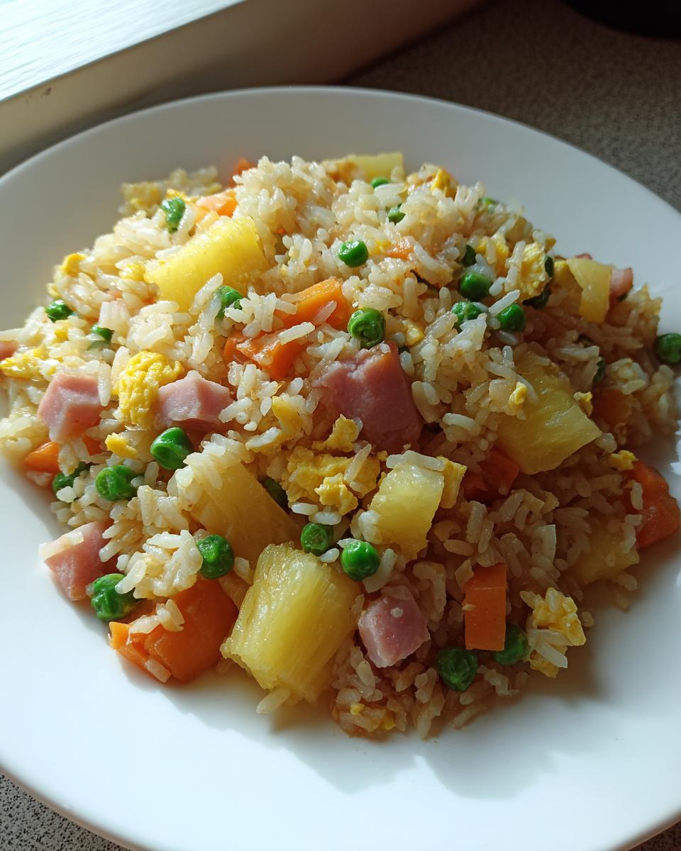 A close-up serving of colorful pineapple fried rice featuring chunks of pineapple, ham, peas, carrots, and scrambled egg.