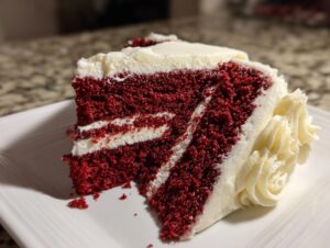 A close-up of a moist slice of red velvet cake showing deep red layers and thick white cream cheese frosting.
