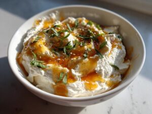 A close-up of a bowl filled with creamy ricotta dip, drizzled with golden honey and topped with fresh herbs and sesame seeds.