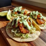 Three delicious shrimp taco shells filled with seasoned shrimp, shredded cabbage, and topped with a creamy green sauce.