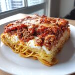 A hearty, square slice of baked spaghetti pie topped with meat sauce and melted cheese.