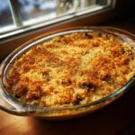 A baked stuffed mushroom dip in a glass dish, featuring a thick, golden brown, crispy breadcrumb topping.