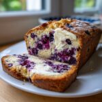 Close-up of a loaf of Blueberry Cream Cheese Bread, sliced, showing rich blueberries and a dollop of melting cream cheese.