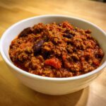 Close-up of a white bowl filled with rich, thick chili featuring ground meat and kidney beans, part of the best chili recipe.