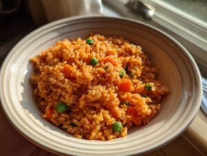 A close-up of a bowl filled with vibrant orange Mexican rice mixed with bright green peas and diced carrots.