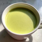 Close-up of bright green, creamy celery soup served hot in a white mug.