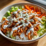 Close-up of a vibrant buffalo chicken bowl featuring shredded buffalo chicken, rice, celery, carrots, ranch, and blue cheese crumbles.