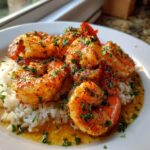 Close-up of perfectly cooked cajun shrimp seasoned with spices and parsley, served over white rice with buttery sauce.