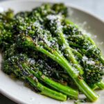 Close-up of bright green, charred broccolini stalks topped generously with grated Parmesan cheese.