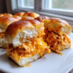 Close-up of two buffalo chicken sliders cut open, showing shredded chicken coated in melted orange cheese sauce.
