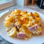 A close-up serving of creamy scalloped potatoes and ham topped with melted cheddar cheese and herbs.