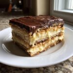 A single serving slice of chocolate eclair cake showing layers of graham crackers, vanilla pudding, and chocolate frosting.