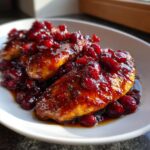 Close-up of two beautifully glazed cranberry chicken breasts topped with a rich, dark cranberry sauce.