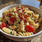 A close-up of a creamy blt pasta salad featuring rotini pasta, bright red cherry tomatoes, and crispy bacon bits.