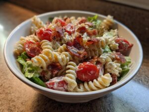 A close-up of a creamy blt pasta salad featuring rotini pasta, cherry tomatoes, lettuce, and crispy bacon pieces.