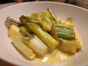 Close-up of tender braised leeks served in a rich, creamy yellow sauce in a white bowl.