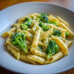 Close-up of creamy broccoli pasta made with penne, bright green florets, and herbs in a white bowl.