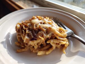 A serving of creamy french onion pasta topped with caramelized onions and melted cheese on a white plate.