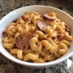 Close-up of creamy, cheesy kielbasa pasta with elbow macaroni and sliced sausage in a white bowl.