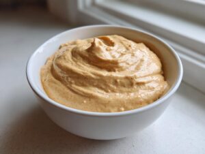 A close-up of a thick, creamy peanut sauce swirled in a white bowl, ready for serving.