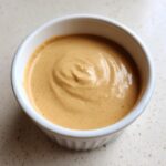 Close-up of creamy, light brown peanut sauce swirled in a small white ramekin.