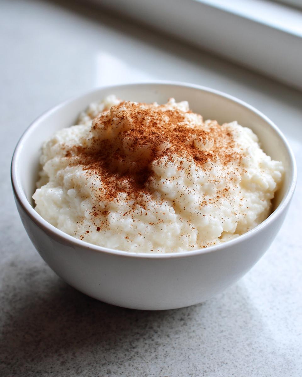 A close-up of creamy rice pudding topped generously with ground cinnamon in a white bowl.