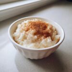 A close-up of creamy rice pudding served in a white bowl, generously dusted with ground cinnamon.