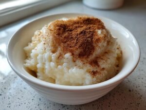 Close-up of creamy white rice pudding served in a white bowl, generously topped with ground cinnamon.