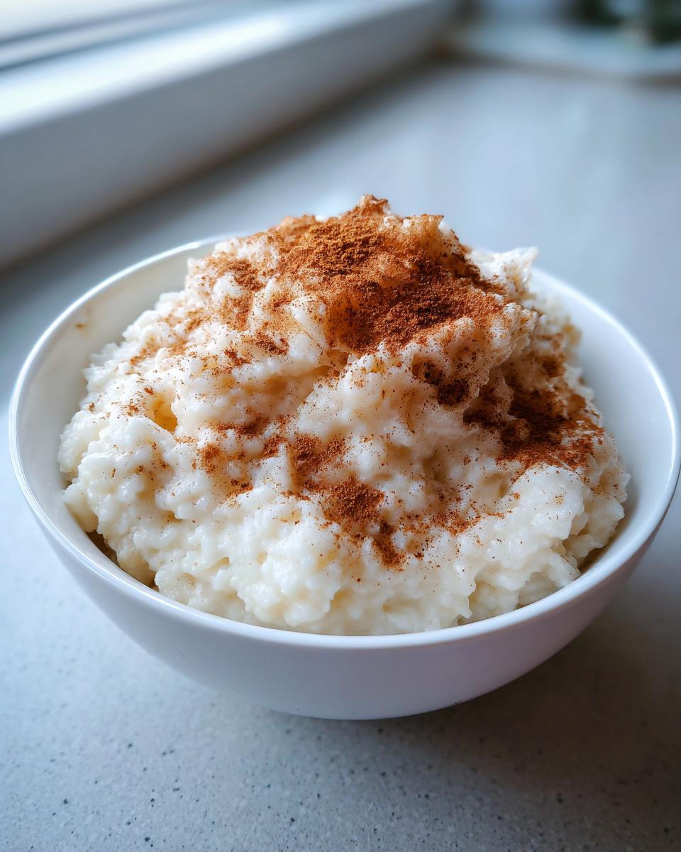 A close-up of creamy rice pudding served in a white bowl, generously topped with ground cinnamon.