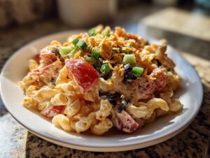 A serving of creamy taco pasta salad featuring elbow macaroni, tomatoes, olives, and topped with crushed chips and green onions.