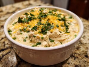 A close-up of creamy white chicken chili topped with shredded cheddar cheese and fresh cilantro.