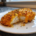 Cross-section of a crispy cheddar chicken breast showing juicy white meat and melted orange cheddar cheese oozing out.