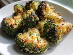 Close-up of crispy, roasted smashed broccoli florets coated in seasoning and cheese on a white plate.