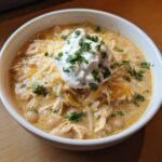Close-up of a bowl of creamy crockpot white chicken chili topped with shredded cheese, sour cream, and cilantro.