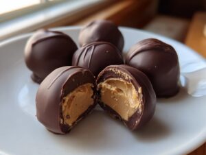 Close-up of chocolate covered peanut butter balls, one cut in half showing the creamy peanut butter filling.